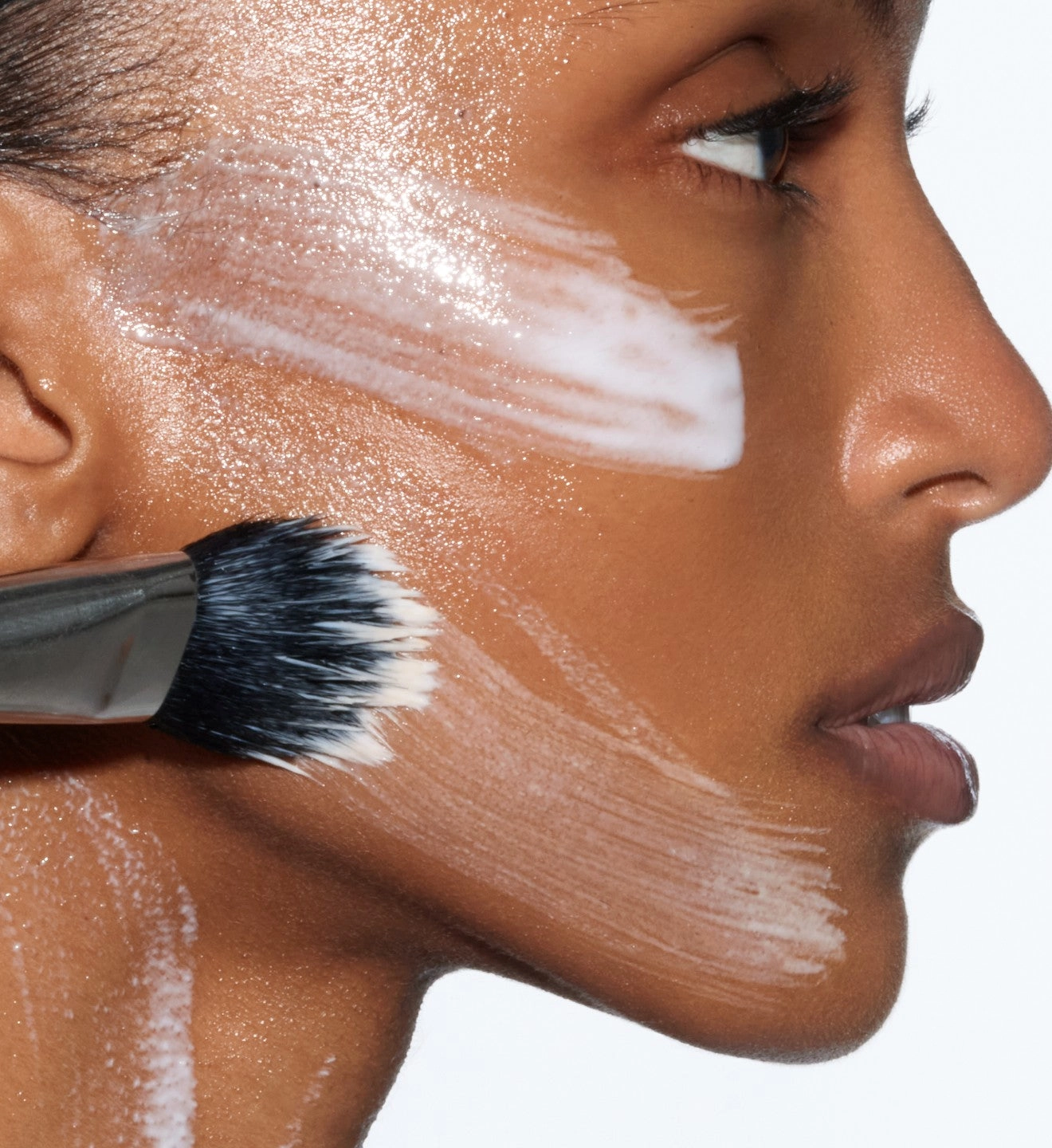 a brush sweeping a pale formula across a cheek in profile